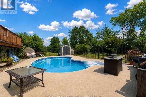 Backyard with a kidney-shaped swimming pool, concrete patio, and a fenced perimeter. - 1848 County Road 9, Greater Napanee