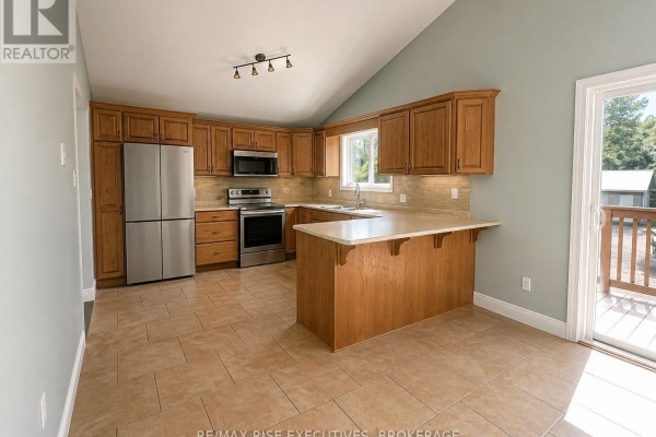 Kitchen with light wood cabinets, stainless steel appliances, and a breakfast bar. - 1848 County Road 9, Greater Napanee