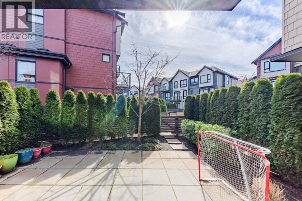 View of a backyard patio with evergreen hedges, a small tree, and a hockey net. - 185 4738 Hemlock Way, Tsawwassen
