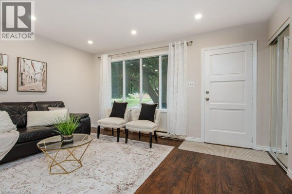 Living room with a black leather sofa, two chairs, a glass coffee table, and a large window. - 185 Cedarvale Crescent Unit# A, Waterloo