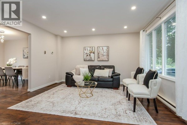 Living room with wood floors, a black sofa, a patterned rug, and a view into a dining area. - 185 Cedarvale Crescent Unit# A, Waterloo
