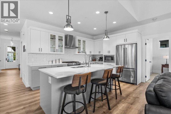 Bright kitchen with white and grey cabinets, quartz countertops, stainless steel appliances, and an island with stools. - 185 Diamond Way, Vernon