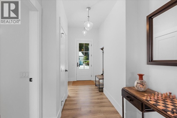 Hallway with white walls, light wood flooring, a glass-paned front door, and a decorative console table. - 185 Diamond Way, Vernon