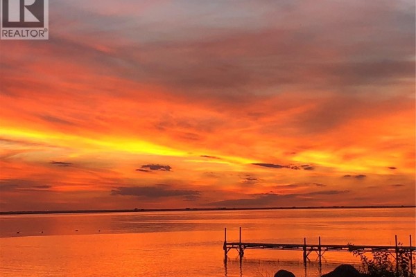 Vibrant orange and yellow sunset over a lake with a wooden dock in the foreground. - 185 Gordon Drive, Last Mountain Lake