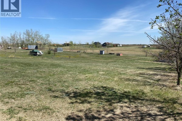 Expansive green field with scattered trees, sheds, and buildings under a clear blue sky. - 185 Gordon Drive, Last Mountain Lake