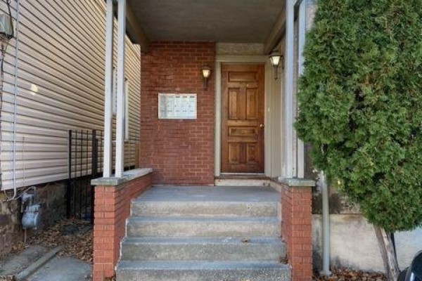 Front porch entrance with brick facade, wooden door, and concrete steps. - 185 James Street, St  Catharines
