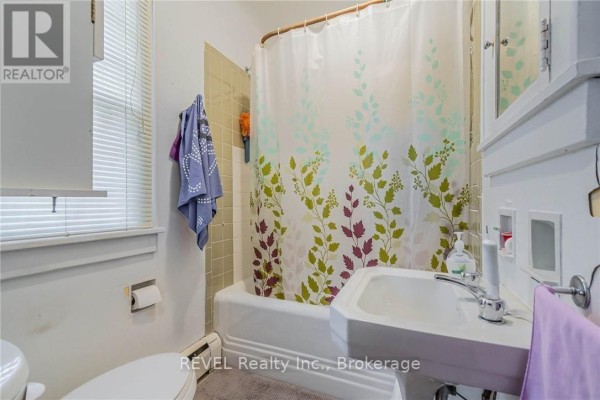 Bathroom with a sink, toilet, bathtub, and shower curtain with a leaf pattern. - 185 James Street, St  Catharines