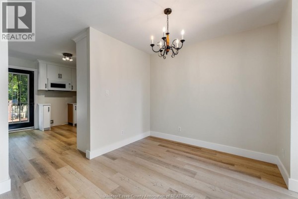 Dining area with light wood floors, cream walls, and view into a white kitchen. - 185 Marlborough Street East, Leamington