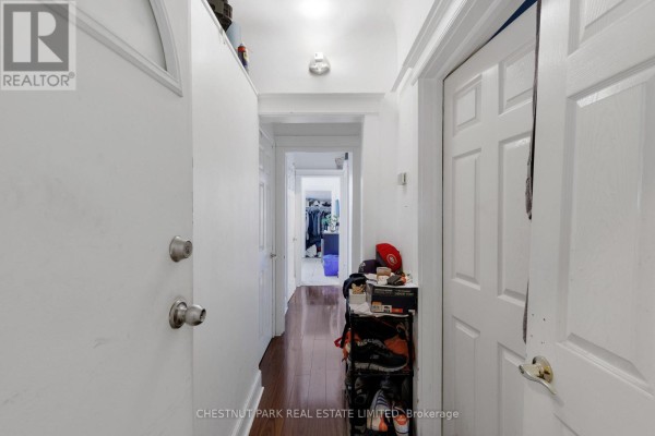 View down a narrow white hallway with wooden flooring and doors on either side. - 185 Walmer Road, Toronto