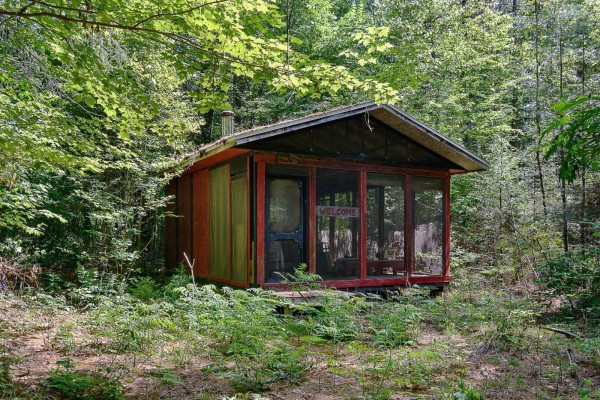 Small wooden cabin with a red-trimmed screened porch nestled amongst trees and undergrowth. - 1851 Ch. De La Rivière-noire, Waltham