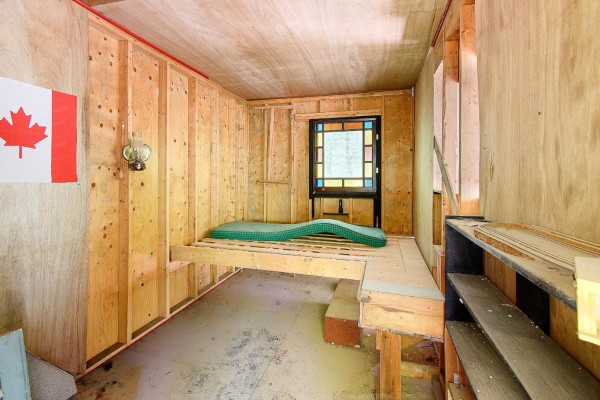 Interior view of a small cabin with unfinished wood walls, a mattress on a raised platform, and shelves. - 1851 Ch. De La Rivière-noire, Waltham