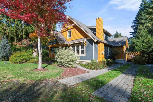 Side exterior view of the house with a stone chimney and paved driveway. - 1852 Ravenwood Trail, Cultus Lake South, Lindell Beach