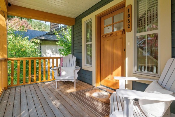 Covered front porch with two Adirondack chairs and a wooden front door. - 1852 Ravenwood Trail, Cultus Lake South, Lindell Beach