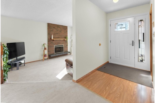 Interior view of a home showing a white front door, wood-look flooring, and a carpeted living room with a brick fireplace. - 18528 98 Av Nw, Edmonton