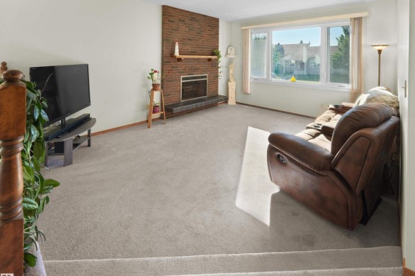 Living room with a brick fireplace, large window, brown leather sofa, and carpet flooring, viewed from the staircase. - 18528 98 Av Nw, Edmonton