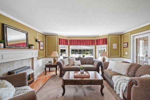 Living room with olive green walls, white wainscoting, a fireplace, and brown upholstered furniture. - 18555 57 Avenue, Surrey