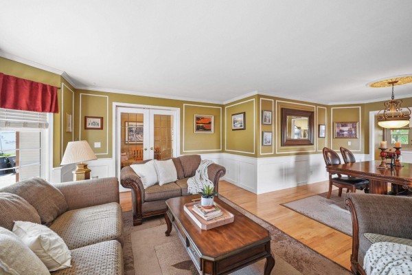 Living room with olive green walls, white wainscoting, and view towards a dining area. - 18555 57 Avenue, Surrey
