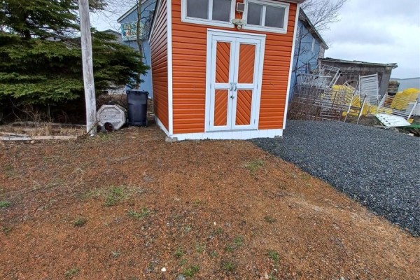 Small orange shed with white trim and double doors, next to a garbage bin and pine trees. - 186 Main Street N, Glovertown