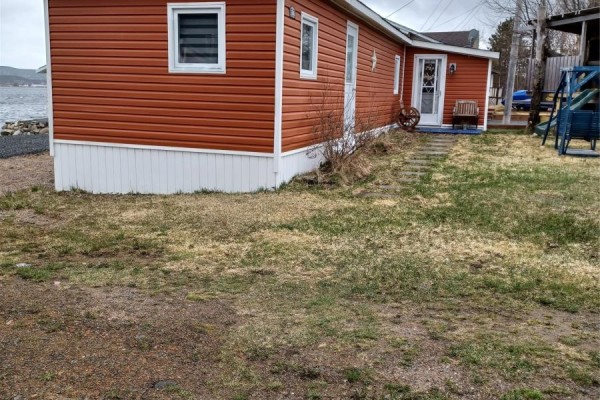 Side exterior of the orange mobile home with a white foundation and a grassy yard. - 186 Main Street N, Glovertown