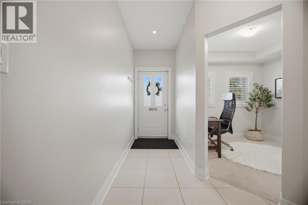 Interior hallway with light gray walls, beige tile floor, and a doorway to an office with a desk. - 1860 Burnhamthorpe Road E, Mississauga