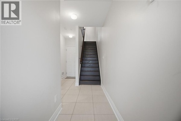 Interior hallway with light gray walls, beige tile floor, and a dark wood staircase leading upwards. - 1860 Burnhamthorpe Road E, Mississauga