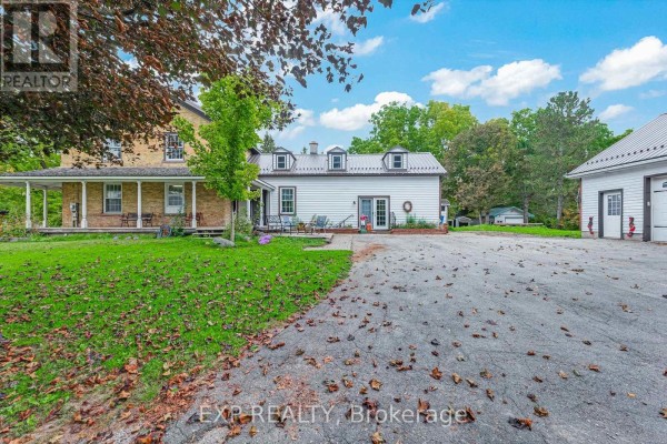 Exterior view of a yellow brick house with a covered porch and attached white siding section, driveway in foreground. - 18611 Leslie Street, East Gwillimbury