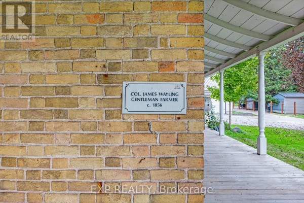 Close-up of a brick wall with a historical plaque and part of a wooden porch. - 18611 Leslie Street, East Gwillimbury