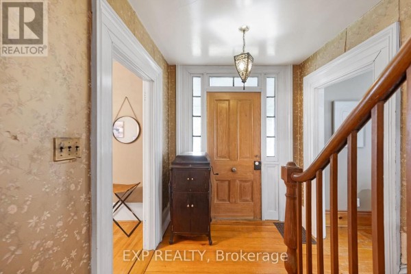 Interior entryway with a wooden front door, staircase, antique cabinet, and patterned wallpaper. - 18611 Leslie Street, East Gwillimbury
