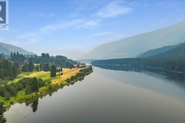 Aerial view of a wide river bordered by a highway, green fields, and dense forest. - 1864 Highway 3a, Castlegar