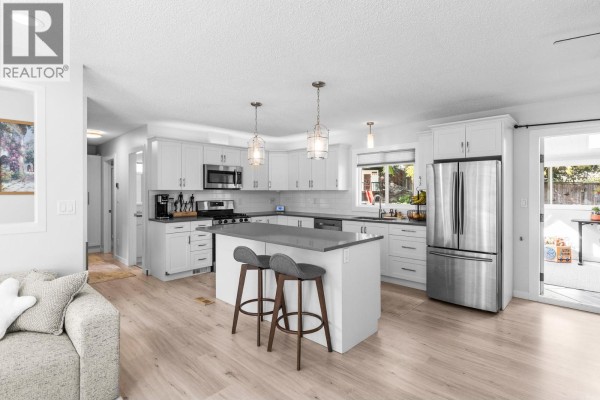 Modern white kitchen with grey island, stainless steel appliances, and light wood flooring. - 1866 Large Avenue, Kelowna