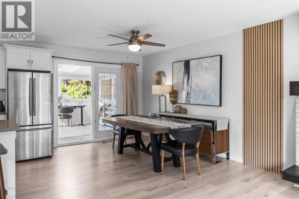 Dining area with a wooden table, sliding glass doors to a patio, and abstract art. - 1866 Large Avenue, Kelowna