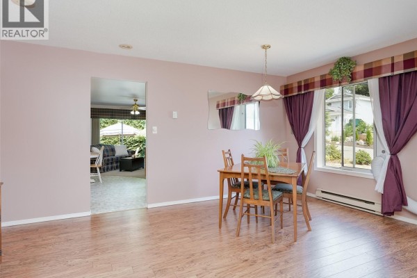 Dining area with wooden table and chairs, view into living room, and window with plaid valance. - 1867 Deborah Dr, Duncan