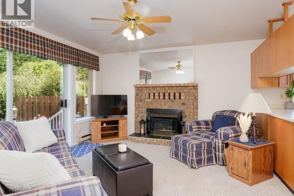 Family room with plaid sofa and armchair, fireplace, television, and wooden cabinetry. - 1867 Deborah Dr, Duncan