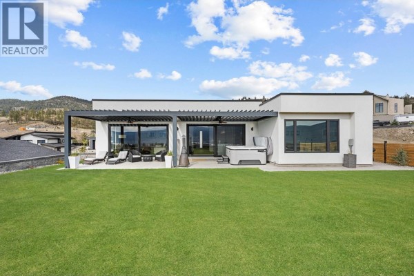 Rear exterior of modern house with large lawn, covered patio, and hot tub. - 18685 Sanborn Place, Summerland