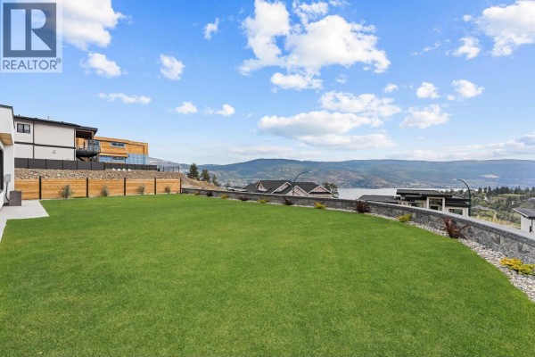 View from backyard showcasing a large green lawn and distant lake and mountain scenery. - 18685 Sanborn Place, Summerland