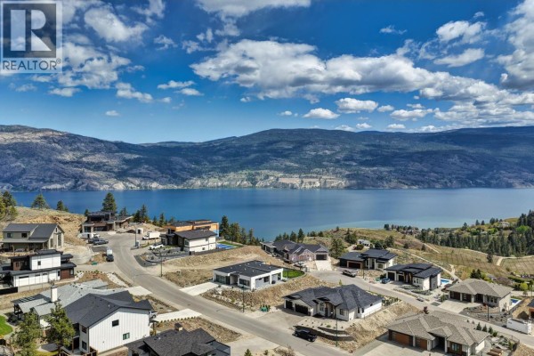 Open concept kitchen and dining area with island, modern furniture, and large windows overlooking a valley. - 18685 Sanborn Place, Summerland