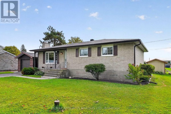 Side view of a brick bungalow with a detached garage and grassy lawn in a rural setting. - 18696 County Road 2 Road, South Glengarry