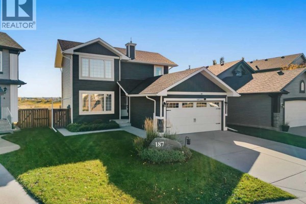Side exterior view of a dark grey two-storey house with a white garage door and green lawn. - 187 Covington Close Ne, Calgary