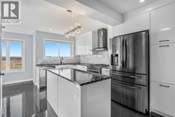 Modern white kitchen with stainless steel appliances, a granite island, and a large window. - 187 Covington Close Ne, Calgary