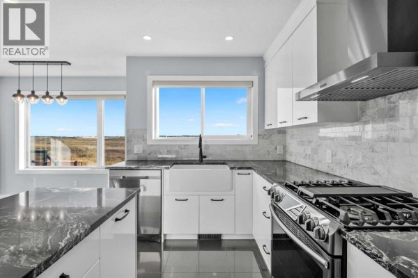 Modern white kitchen with stainless steel appliances, a farmhouse sink, and a large window. - 187 Covington Close Ne, Calgary