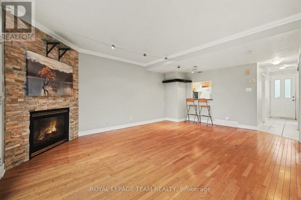 Living room with a stone fireplace, hardwood floors, and view into the kitchen area. - 187 Monterey Drive, Ottawa
