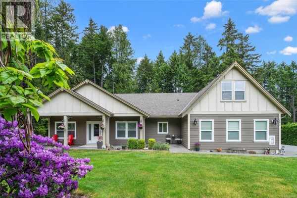 Front exterior of a single-story house with a covered porch, green lawn, and garage. - 1871 Highland Ridge Rd, Shawnigan Lake