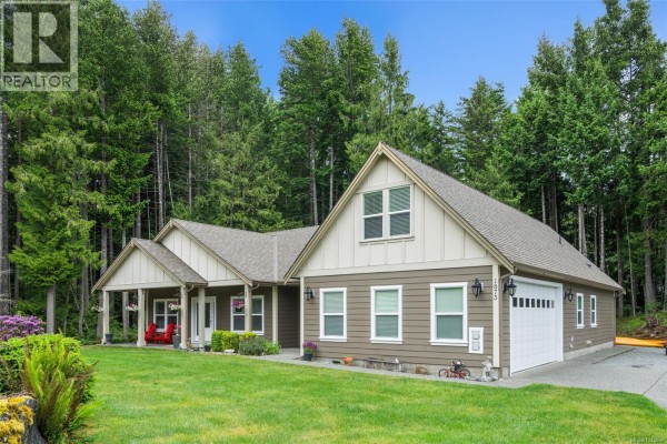 Front exterior of a single-story house with a covered porch, blooming purple flowers, and green lawn. - 1871 Highland Ridge Rd, Shawnigan Lake