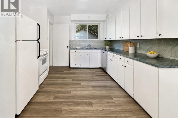 Kitchen with white appliances, white cabinets, and dark countertops. - 1872 101st Street, North Battleford