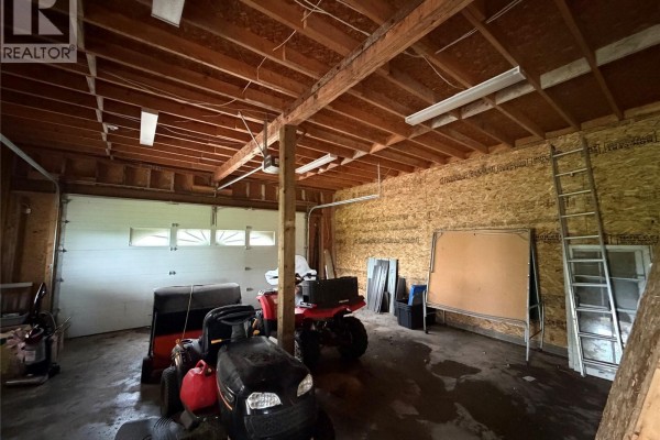 Interior of a garage showing a lawn tractor, ATV, ladder, and unfinished plywood walls and ceiling. - 188 Centre Street, Hudson Bay Rm No  394