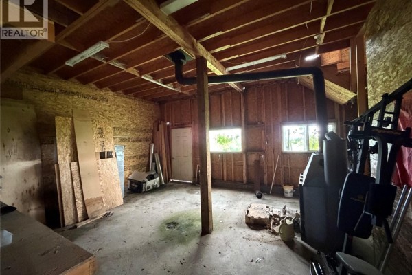 A view inside a garage with wood paneling, two windows, a wood stove, and exercise equipment. - 188 Centre Street, Hudson Bay Rm No  394