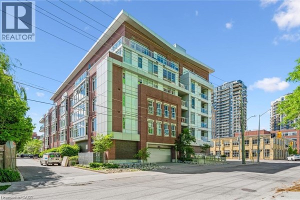 Rear exterior of the apartment building with a garage door and surrounding trees. - 188 King Street S Unit# 304, Waterloo