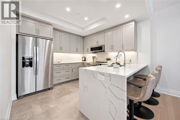 Modern kitchen with light gray cabinets and a waterfall island with bar stools. - 1880 Gordon Street Unit# 707, Guelph