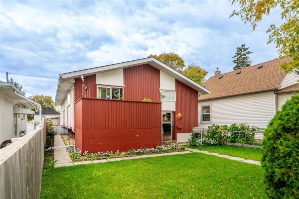 Side view of a red and white split-level house with green lawn and surrounding fence. - 1884 Ross Avenue W, Winnipeg