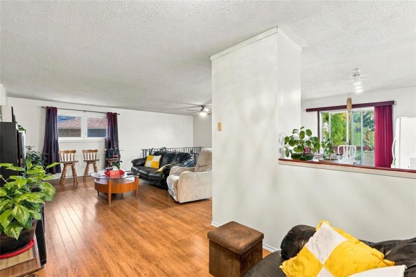 Living room with wood floors, leather sofas, coffee table, and a view into the kitchen area with sliding glass doors. - 1884 Ross Avenue W, Winnipeg